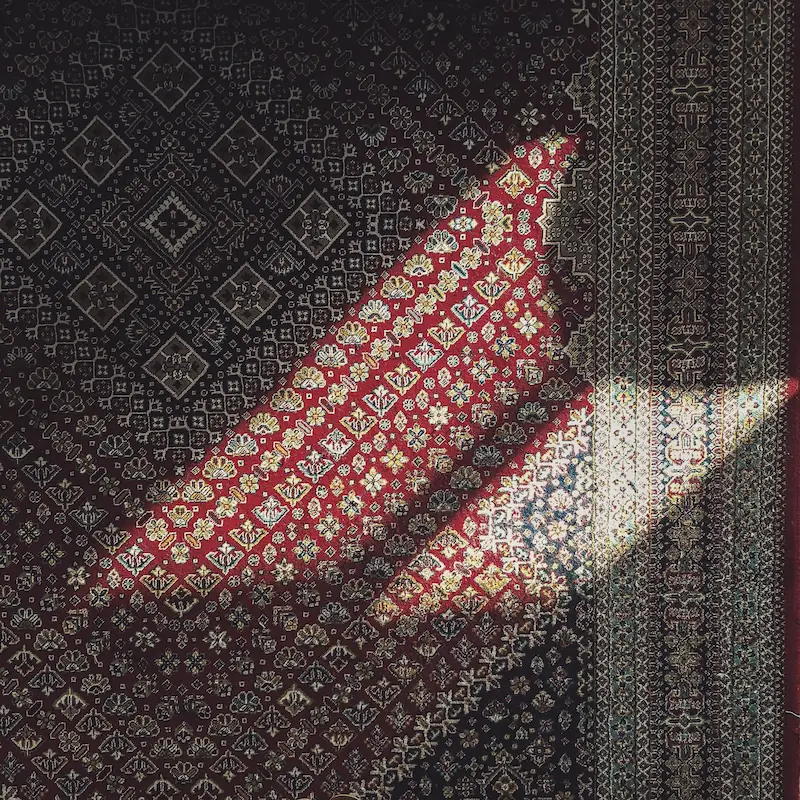 A Persian carpet with a diagonal shaft of sunlight across it.