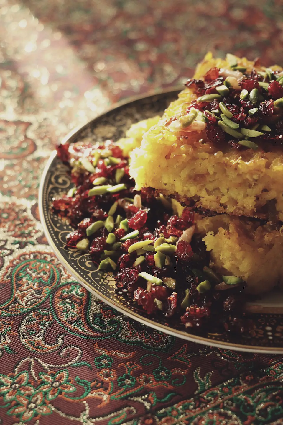 Saffron rice tahchin topped with barberries and pistachios, on an embroidered cloth.