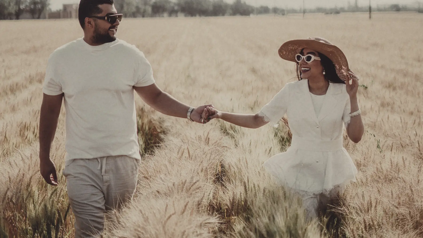 A woman runs through a wheat field holding a man's hand, looking back at him.