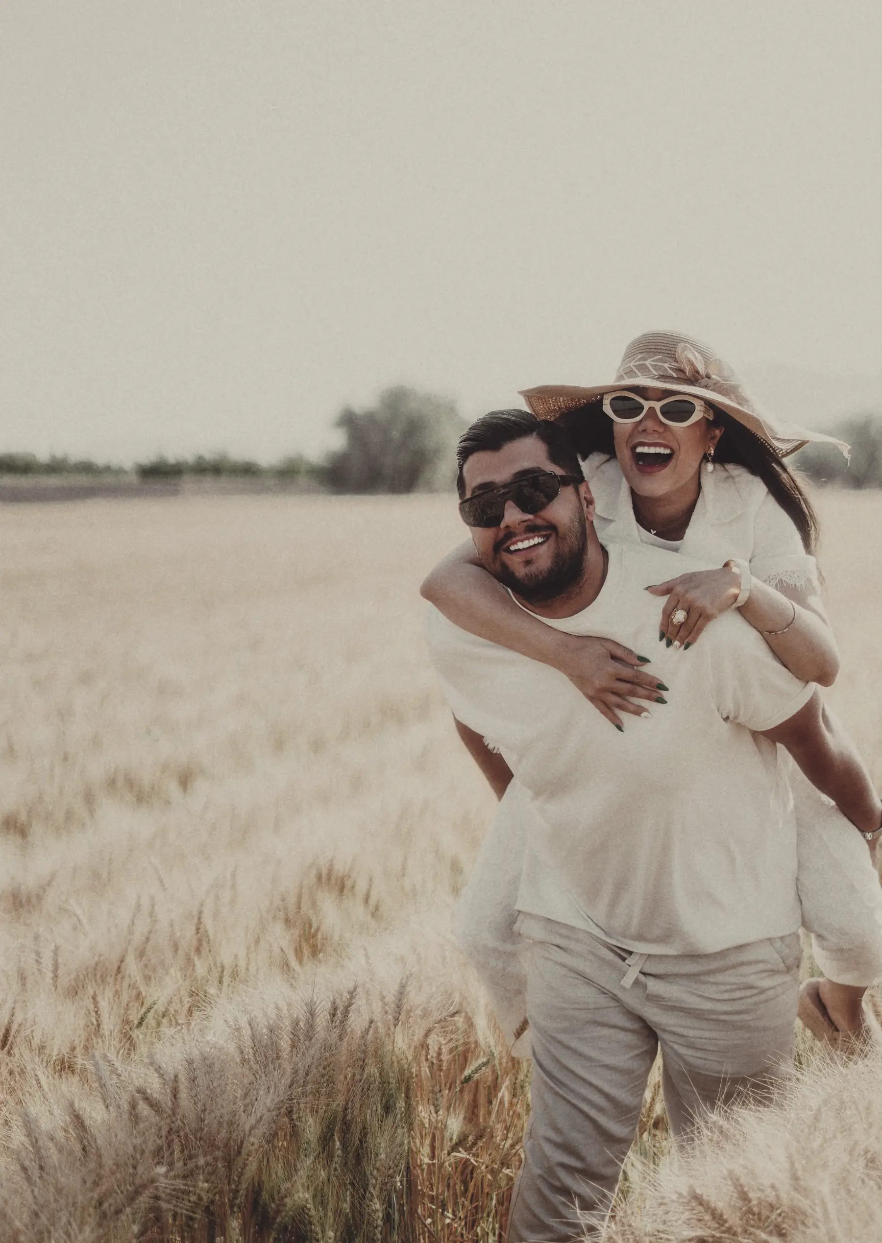 A man carrying a woman piggyback through a wheat field, both laughing.
