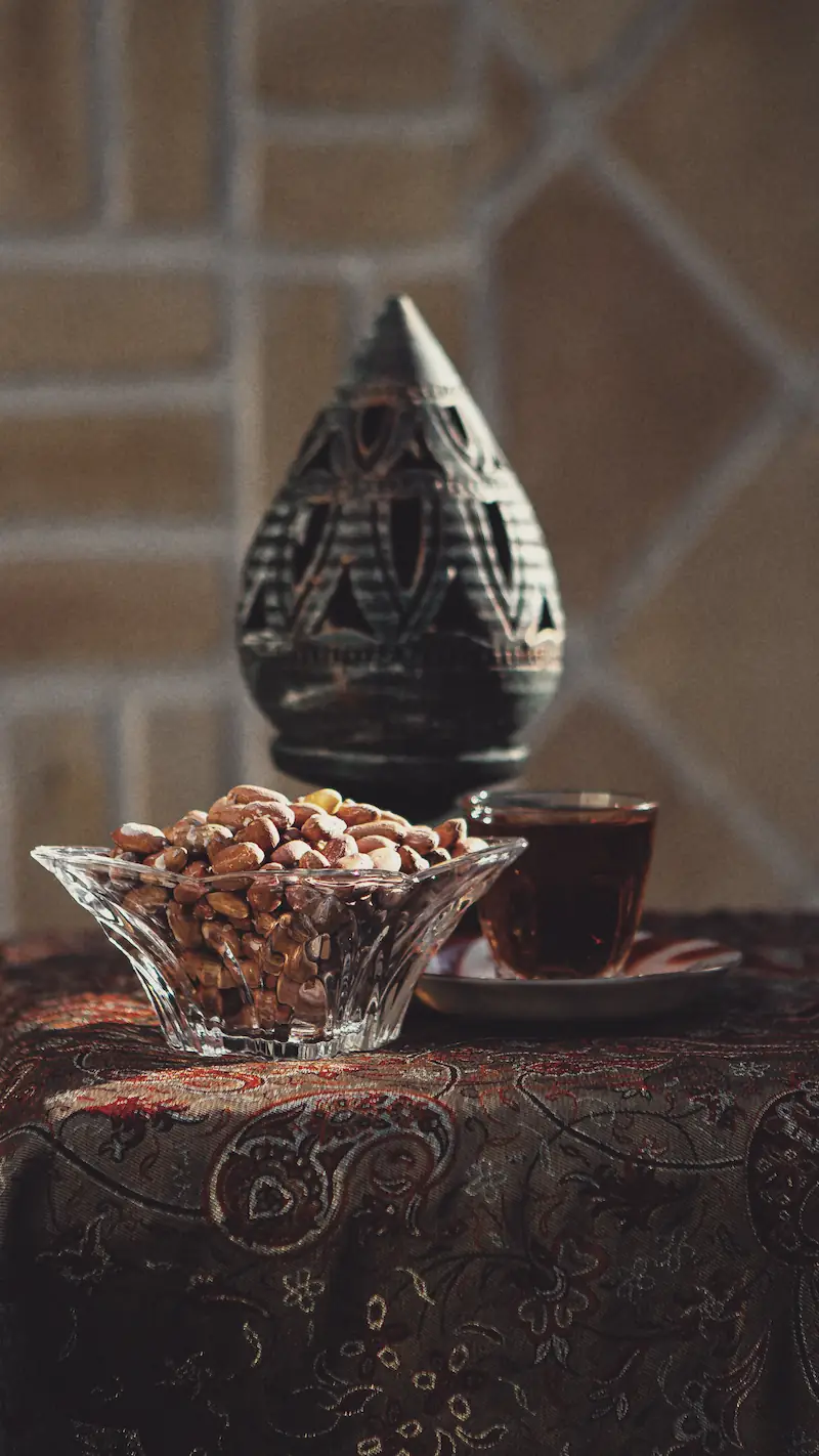 Tea and a bowl of nuts on an embroidered termeh cloth, seen from the table.